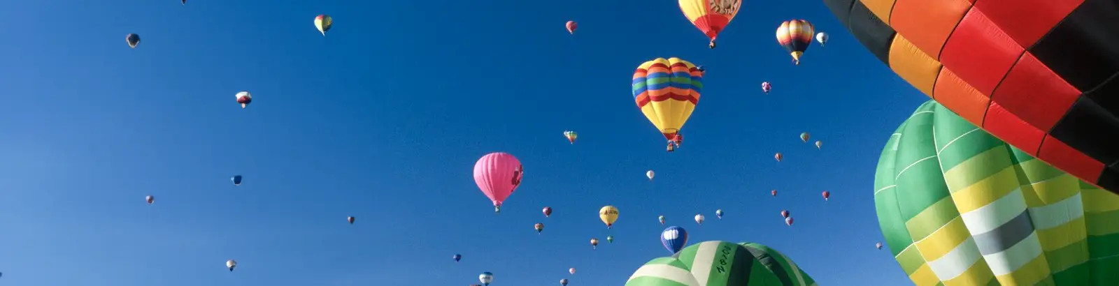 Fotografie einer Vielzahl bunter Heißluftballons schwebt am satt blauen Himmel.