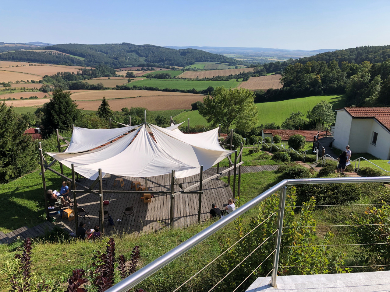 Bild des Veranstaltungsortes Einbecker Sonnenberg, man sieht eine Sonnenterrasse mit einem runden Sonnensegel darüber gespannt im Hintergrund sind Wälder und sanfte Hügel und Felder