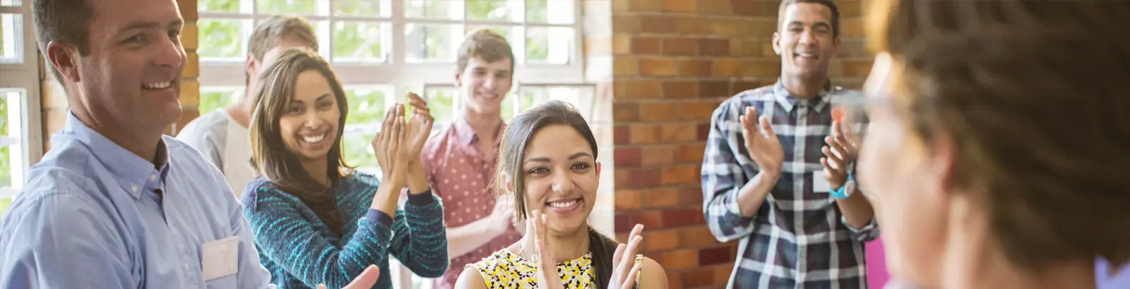 Freudestrahlende Personen applaudieren in einem Seminarraum.
