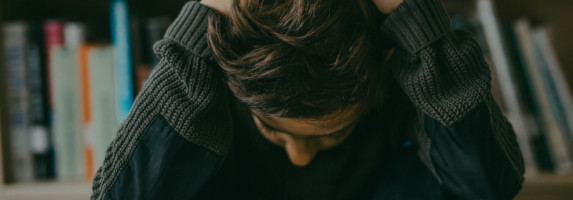 Ein Kind sitzt in einer Bücherei auf dem Boden und hat die Arme über dem Kopf verschränkt und blickt nach unten