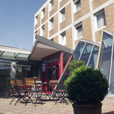 Fotografie des Innenhofes der Hoffmanns Höfe mit Gebäuden im Hintergrund. Eine Gartengarnitur steht in der Sonne auf einer gepflasterten Terrasse, vor der ein runder Busch in einem Kübel zu sehen ist.