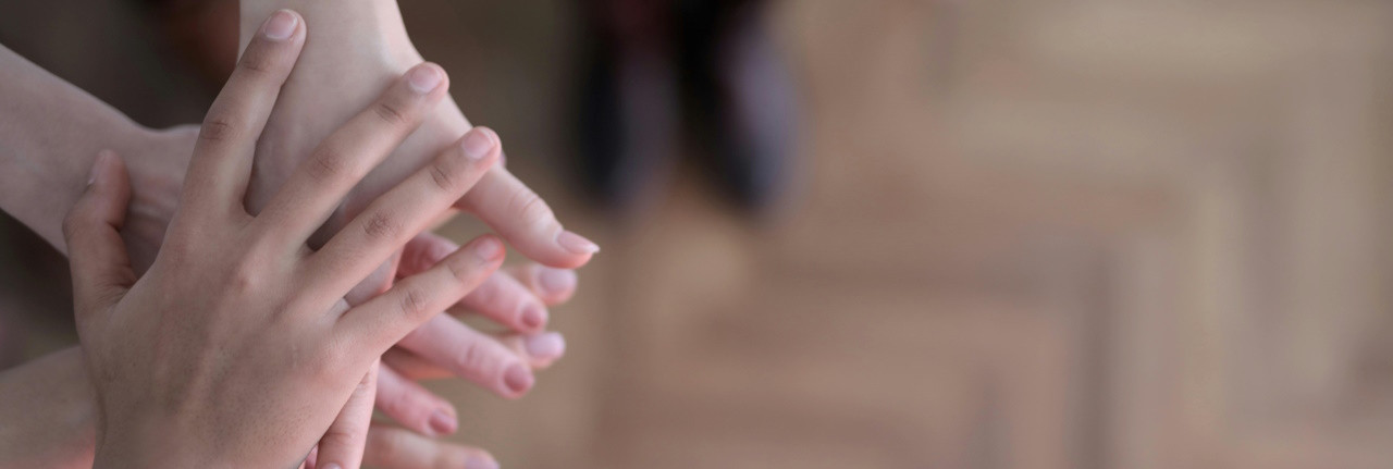 Zeigt vier übereinanderliegende Hände vor einem verschwommenen Hintergrund