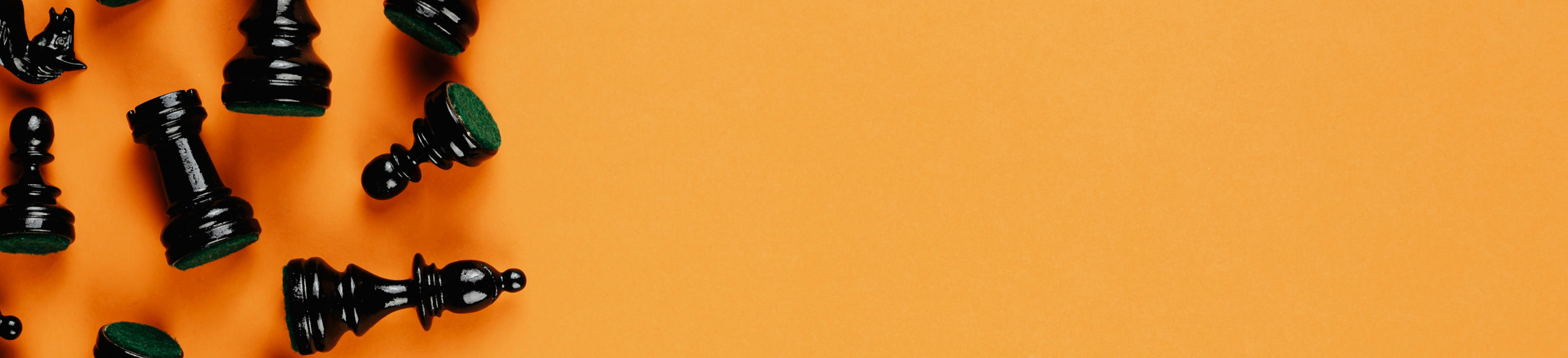 Auf organenem Hintergrund liegen auf der linken Bildseite schwarze Schachfiguren